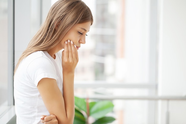 Woman suffering from toothache and touching her cheek while sitting at her desk