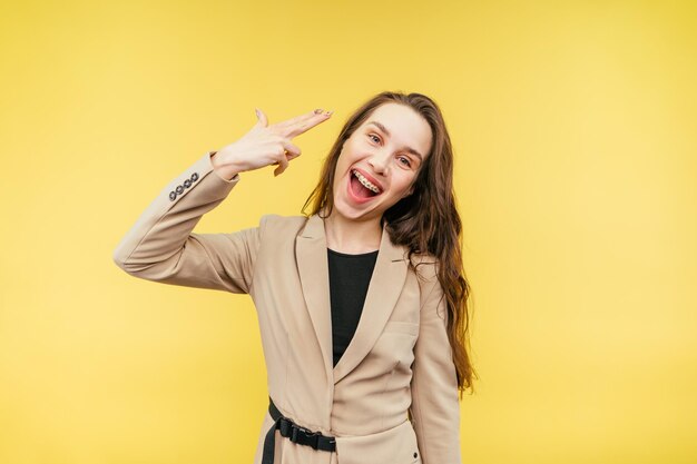 Photo woman in a suit stands on a beige background and shows a gesture of suicide shoots a finger