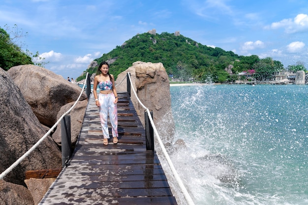 Woman in summer clothing standing on wooden bridge at Nangyuan island with splash sea wave beside, beautiful sea view, place for tourist destination at Suratthani, Thailand