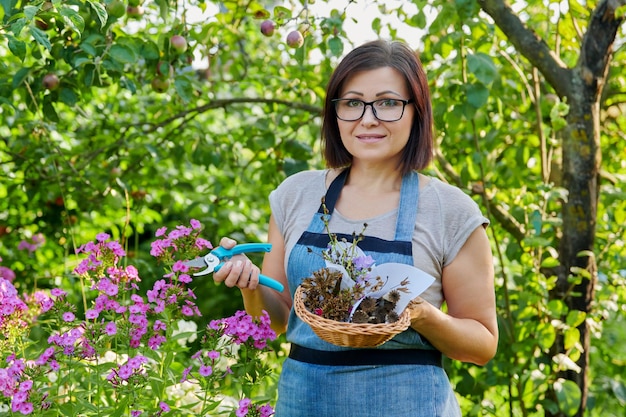 Woman in summer garden with collected dried flowers plant seeds in basket