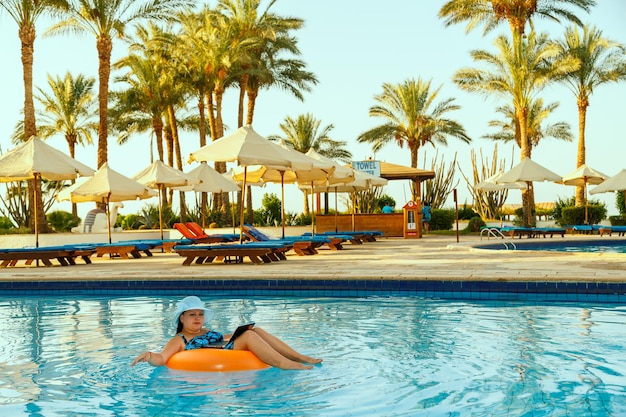 A woman in a sun hat in the pool in a swimming circle with a laptop works remotely