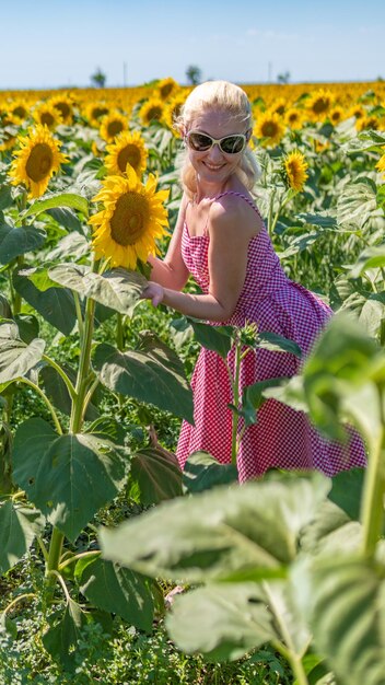 Woman in sunflowers in a red plaid dress with sunglasses a beautiful blonde in the heat