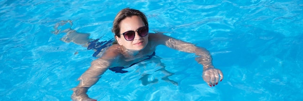 Woman in sunglasses swims in pool in summer