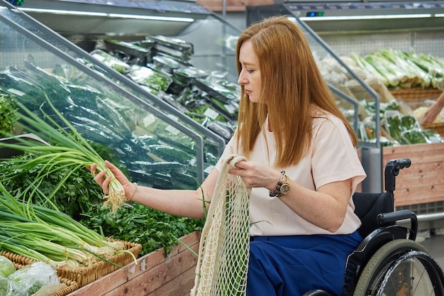 Woman in a supermarket shopping for vegetables while sitting in a wheelchair