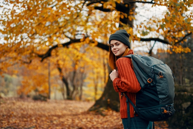 Woman in a sweater cap with a backpack on nature in the forest landscape and fallen leaves High quality photo