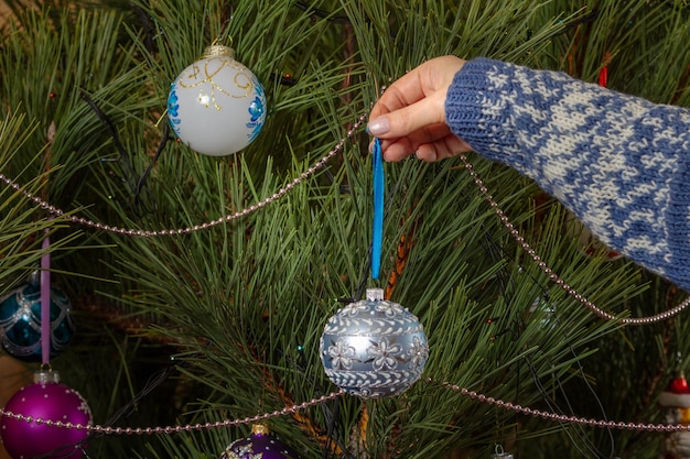 Woman in sweater decorating Christmas tree with toy balls