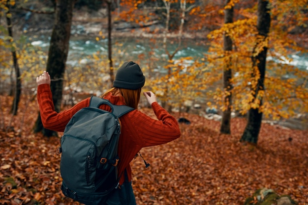 Photo woman in a sweater with a backpack and in jeans walks through the autumn forest in the mountains near the river high quality photo