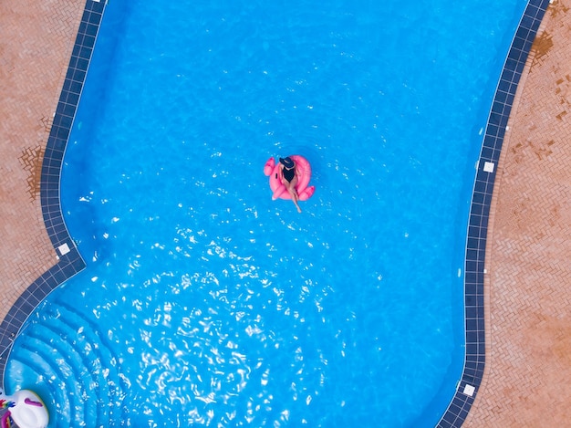 Woman swimming on flamingo pool float in big luxurious pool, drone aerial view