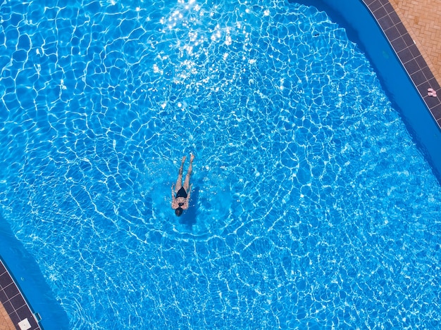 Woman swimming in pool from above view, aerial top view from drone, summer relaxation in hotel