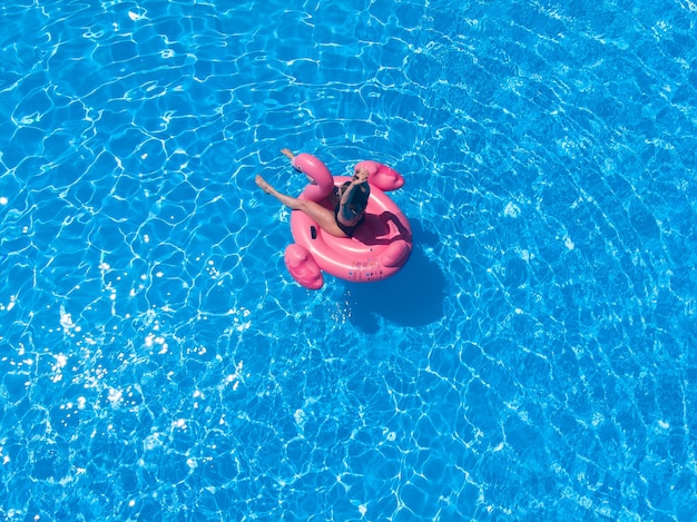 Woman swimming with pink flamnigo in pool from above view, aerial top view from drone, summer relaxation in hotel