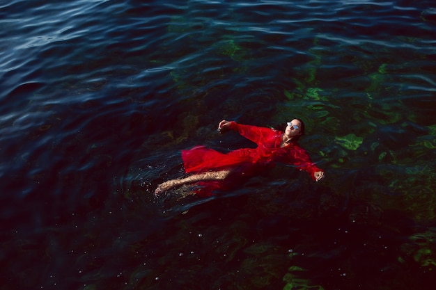 Photo woman swims in the sea in a red long dress with sunglasses in summer