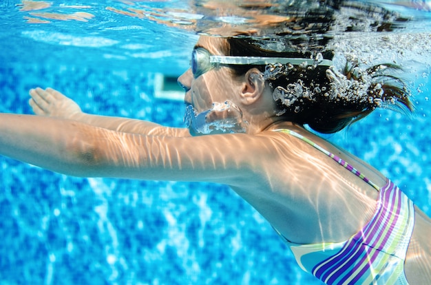 woman swims underwater in swimming pool, happy active teenager girl dives and has fun under water, kid fitness and sport on family vacation on resort