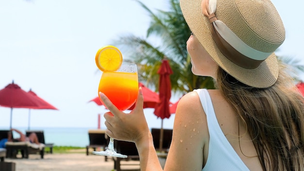 Woman in swimsuit fun in swimming pool drinking tropical orange cocktail