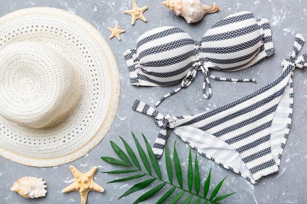 Woman swimwear and beach accessories flat lay top view on colored background Summer travel concept bikini swimsuit straw hat and seasheels Copy space Top view