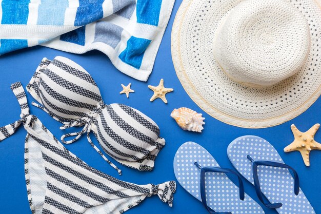 Woman swimwear and beach accessories flat lay top view on colored background Summer travel concept bikini swimsuit straw hat and seasheels Copy space Top view