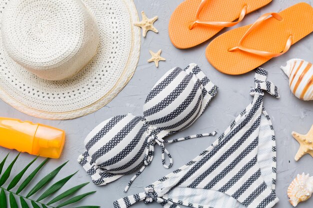 Woman swimwear and beach accessories flat lay top view on colored background Summer travel concept bikini swimsuit straw hat and seasheels Copy space Top view