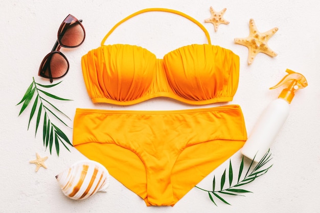 Woman swimwear and beach accessories flat lay top view on colored background Summer travel concept bikini swimsuit straw hat and seasheels Copy space Top view