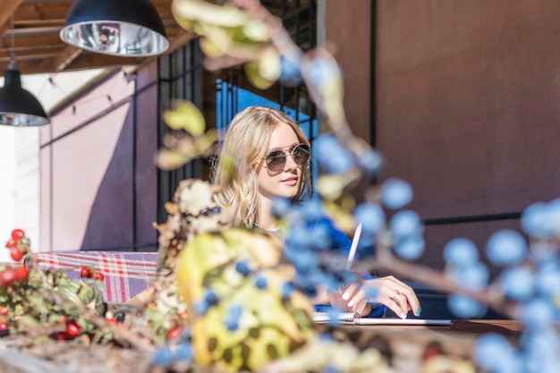 Woman at a table with a pen and notebook, behind blurred autumn bushes