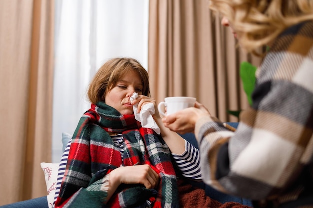 Woman takes care of her daughter who has the flu gives her hot tea to drink