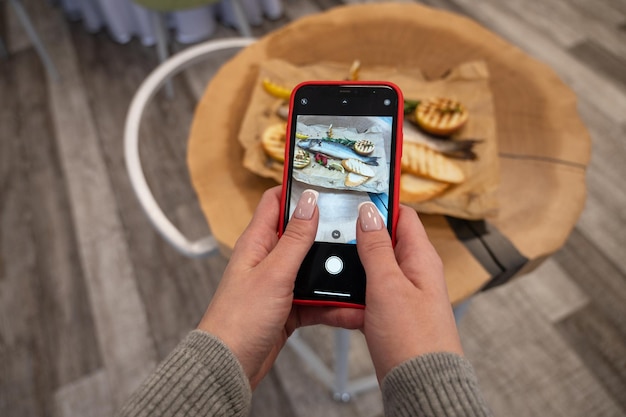 Woman takes photo of sibas fish with greens and vegetables on a wooden background