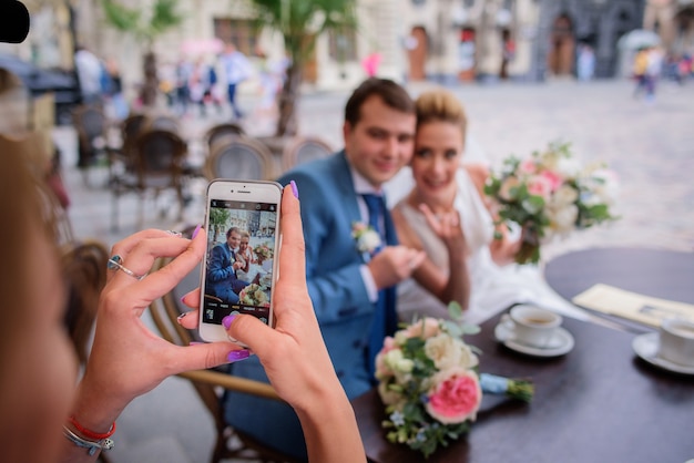 Woman takes a picture of stunning newlyweds sitting in the cafe