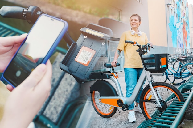 Woman takes a rented bicycle in a bicycle parking with a smartphone