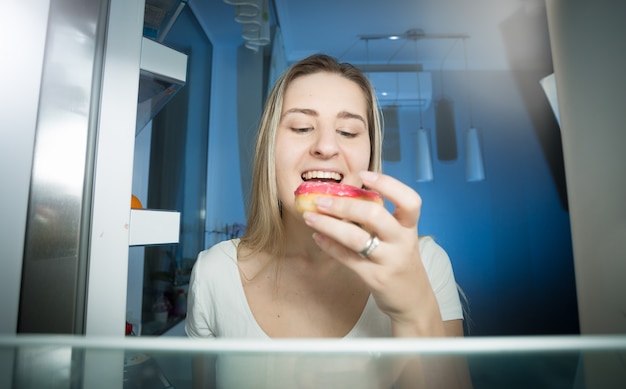 Woman taking donut from refrigerator shelf at late evening