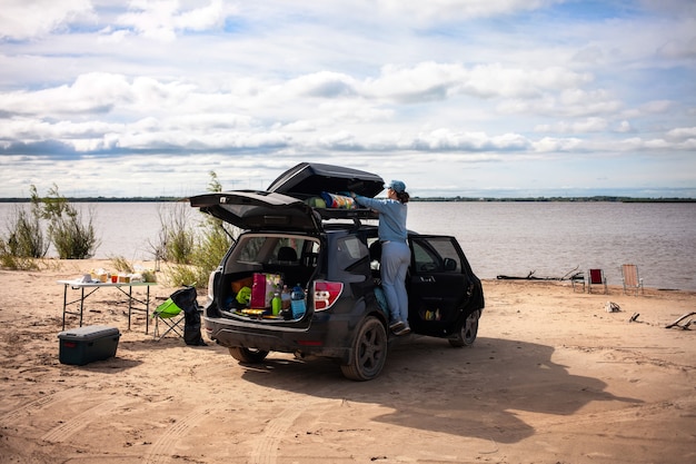 Woman taking off tourist equipment from roof box at the river