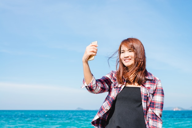 Woman taking selfie using smartphone at sea travel lifestyle.