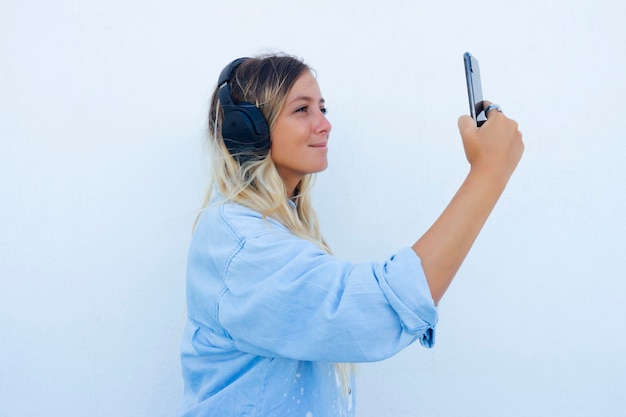 Woman taking a selfie while listening to music on the phone. White background