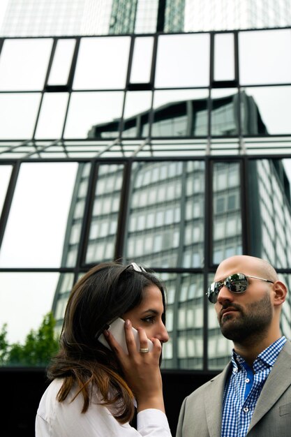 Woman talking to cellphone and business man in front of glass building Photo