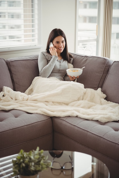 Woman talking on mobile phone while eating breakfast