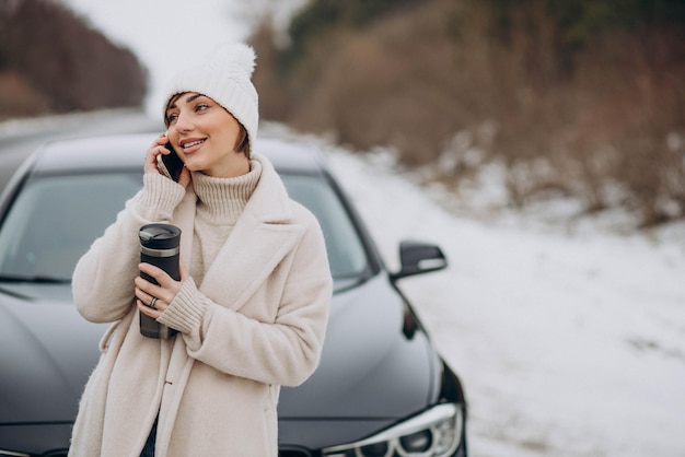 Woman talking on the phone by her car on the road in winter forest