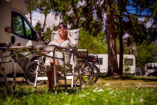 Woman talking on smart phone outdoors in a campsite for holidaymakers. Caravan car Vacation. Family vacation travel, holiday trip in motorhome RV. Connection information communication technology.