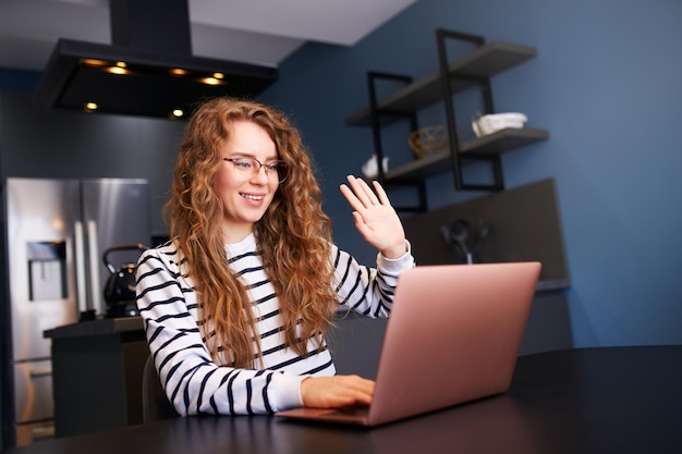 Woman talking on video chat conference with friends on laptop webcam sitting on sofa in living room at night Girl gossips on video call from home Female speak on remote job interview