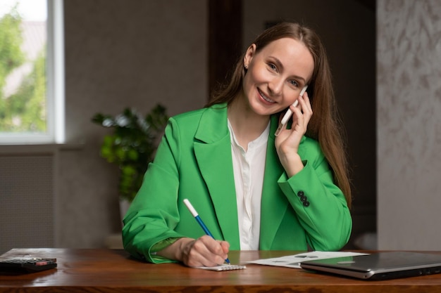 Woman talks to client via mobile phone writing notes