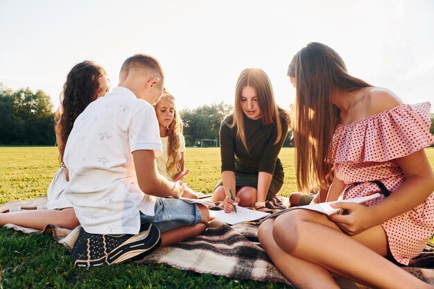 Woman teaching how to draw Group of happy kids is outdoors on the sportive field at daytime