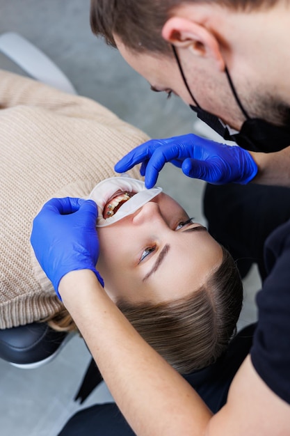 Woman teeth with braces on white teeth. An orthodontist uses dental instruments to place braces on a patient's teeth. The concept of dentistry, orthodontic treatment. Selective focus