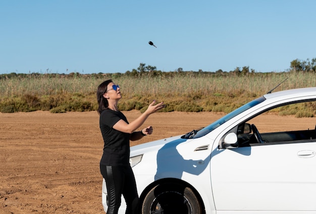 Woman throwing the keys of a car in the air on a dirt road