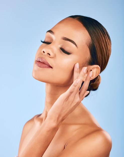 Woman touch face and beauty makeup and skincare with shine and manicure isolated on blue background Female model hand with dermatology and facial healthy skin glow and cosmetic care in a studio