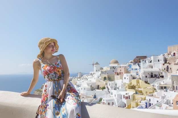 Woman tourist in flora dress visiting whitewashed village in Oia, Santorini Greece. mediterranean sea.