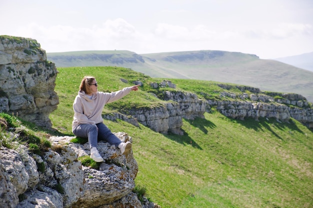 A woman tourist sits on the rock and pointing into the distance by her hand