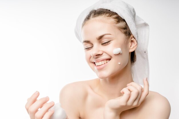 A woman in a towel on the head happy cleanses the skin with foam on a white background isolated. Skincare cleansing concept,copyspace