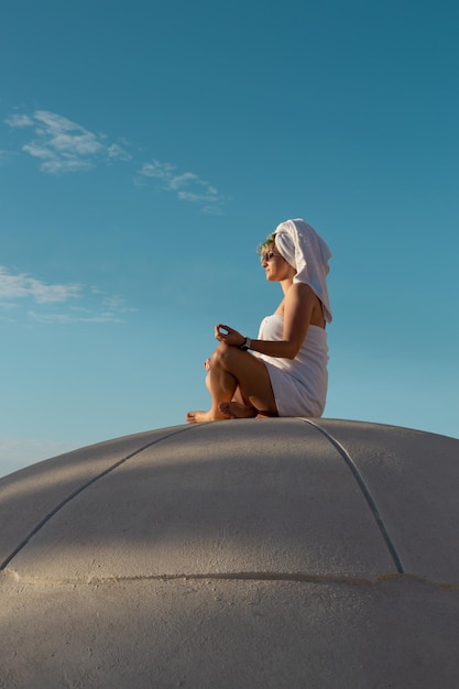 A woman in a towel meditating and greeting the morning on the roof of a spherical building