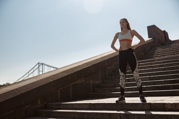 Woman in tracksuit stands on stone steps on city embankment