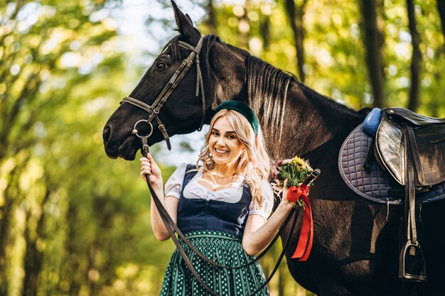 Woman in traditional dress walking with a horse in the forest