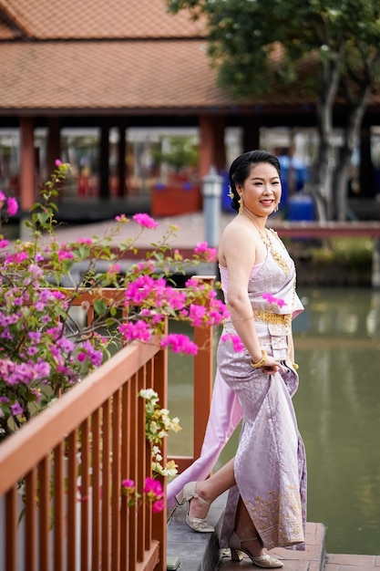 Photo a woman in a traditional thai costumes is standing on the wooden bridge while being taken a portrait photo shooting