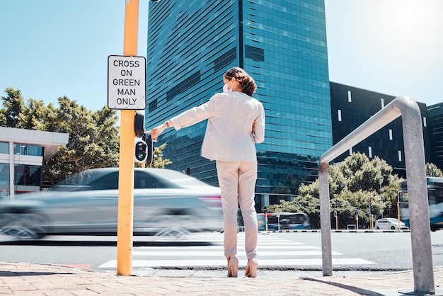 Woman traffic light button and city road waiting to cross pedestrian to walk or commute to work office building Female with covid mask at crosswalk by asphalt street while traveling in south africa