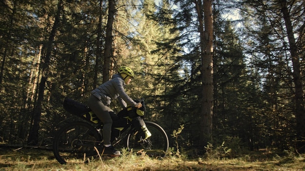 The woman travel on mixed terrain cycle touring with bike bikepacking. The traveler journey with bicycle bags. Magic forest park.