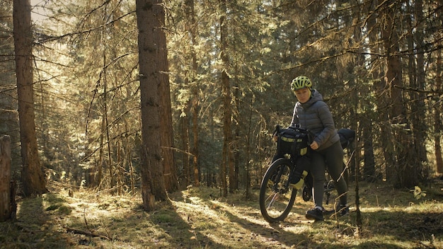 The woman travel on mixed terrain cycle touring with bike bikepacking. The traveler journey with bicycle bags. Magic forest park.